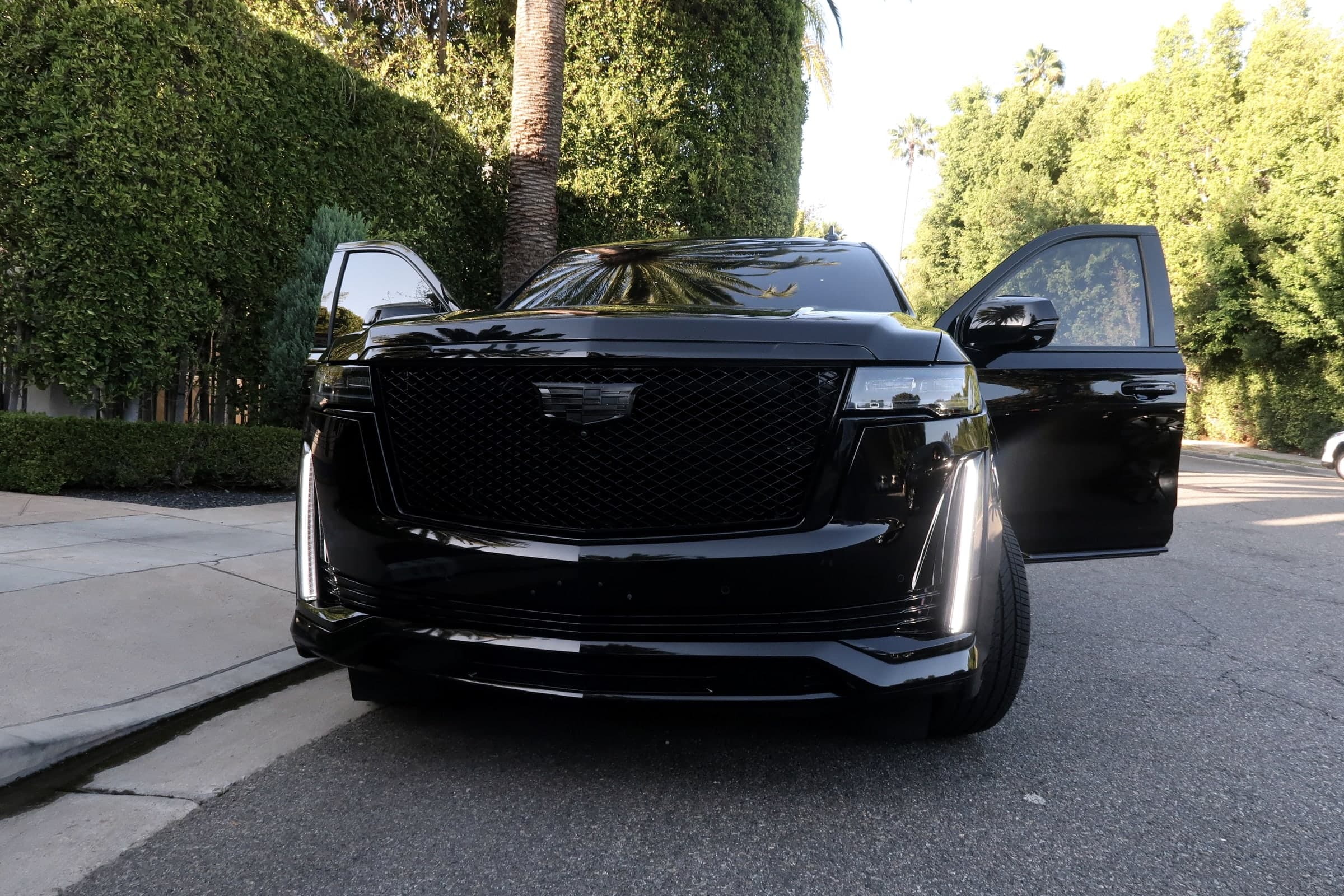 Black Cadillac Escalade with its front doors open, ready for passengers at the curb