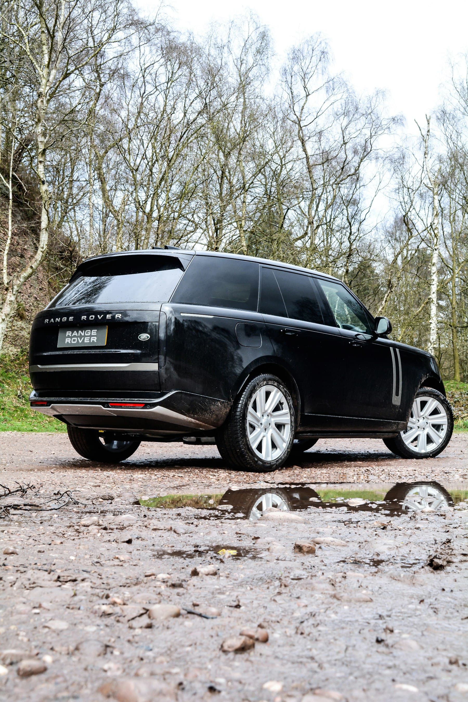 Black Range Rover, three-quarter rear view on a wet gravel road at dusk, Los Angeles